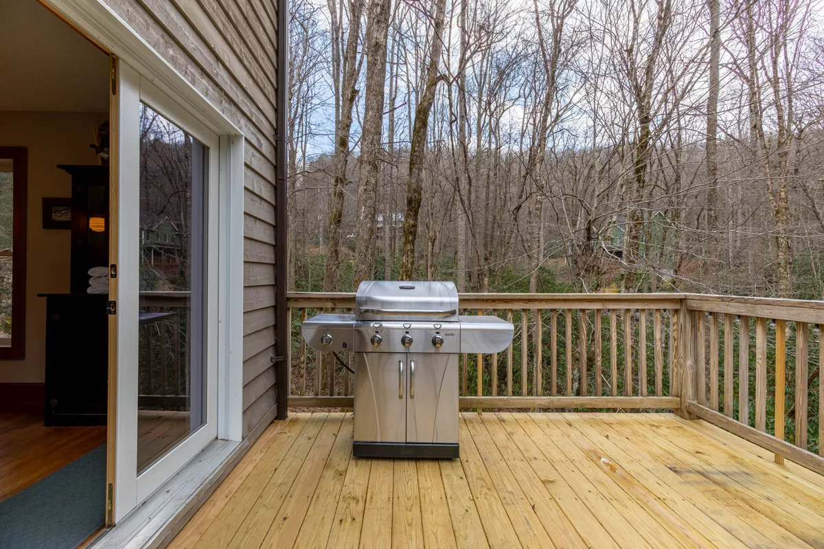 A cozy view of the deck's gas grill set against a backdrop of towering pines and natural greenery. The scene suggests the joy of barbecuing and outdoor gatherings, with space to relax and connect with friends or family.