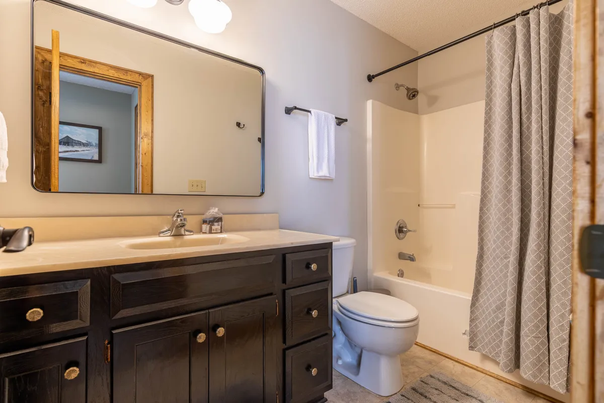 A bathroom featuring a dark wood vanity, large mirror, shower curtain, and updated bath fixtures. The space is bright, clean, and designed for relaxation and refreshing routines.