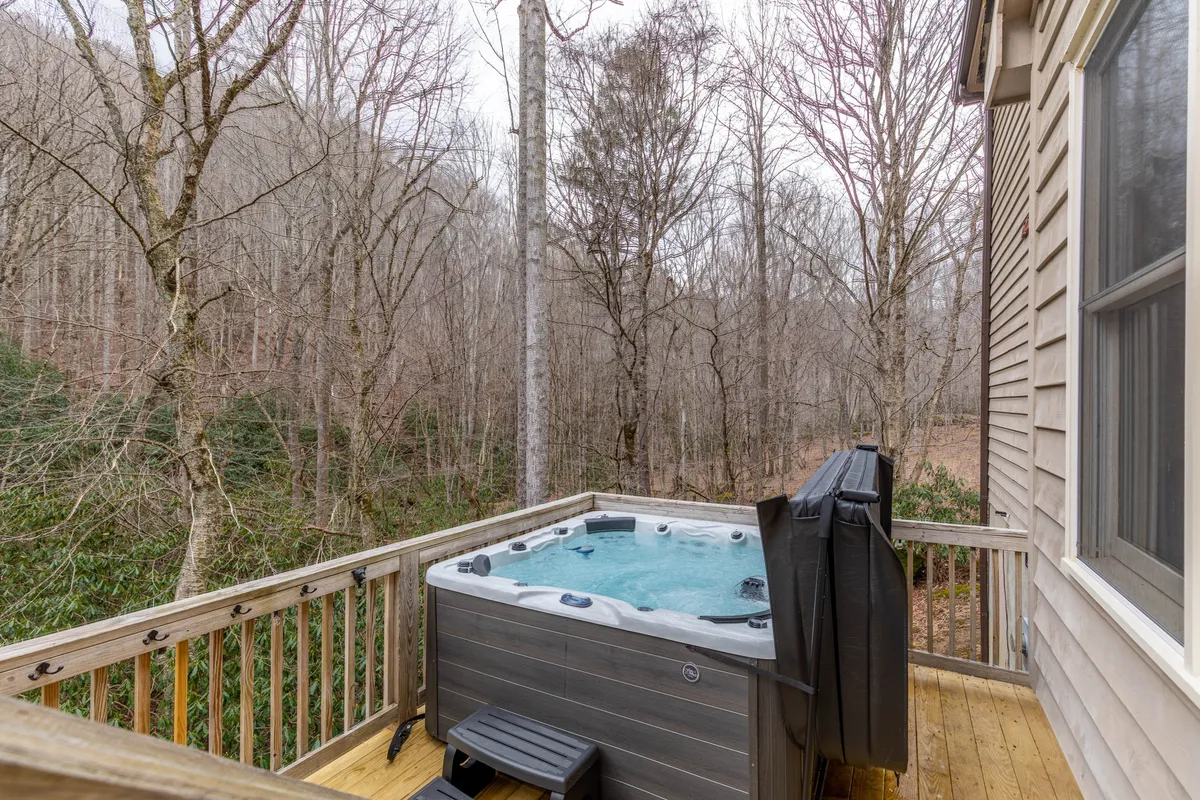 A close-up of the deck’s hot tub, surrounded by lush trees and wooden decking, evoking a sense of privacy and connection with nature. The bubbling water and serene setting highlight the rejuvenating experience of a private soak.