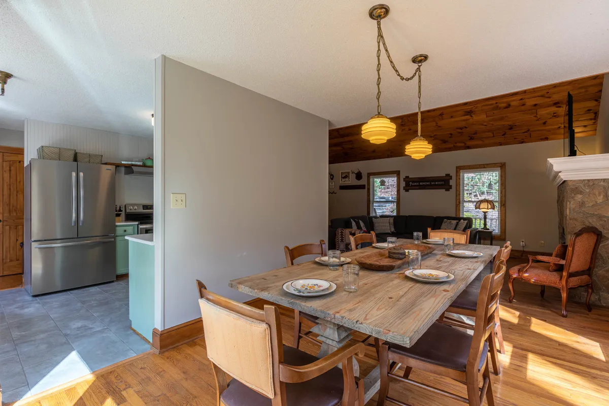 A cozy interior image featuring a spacious dining table, warm lighting fixtures, and a stone fireplace. This welcoming atmosphere sets the stage for family dinners, gatherings, and celebratory toasts in a comfortable, home-like setting after a day of mountain exploration.