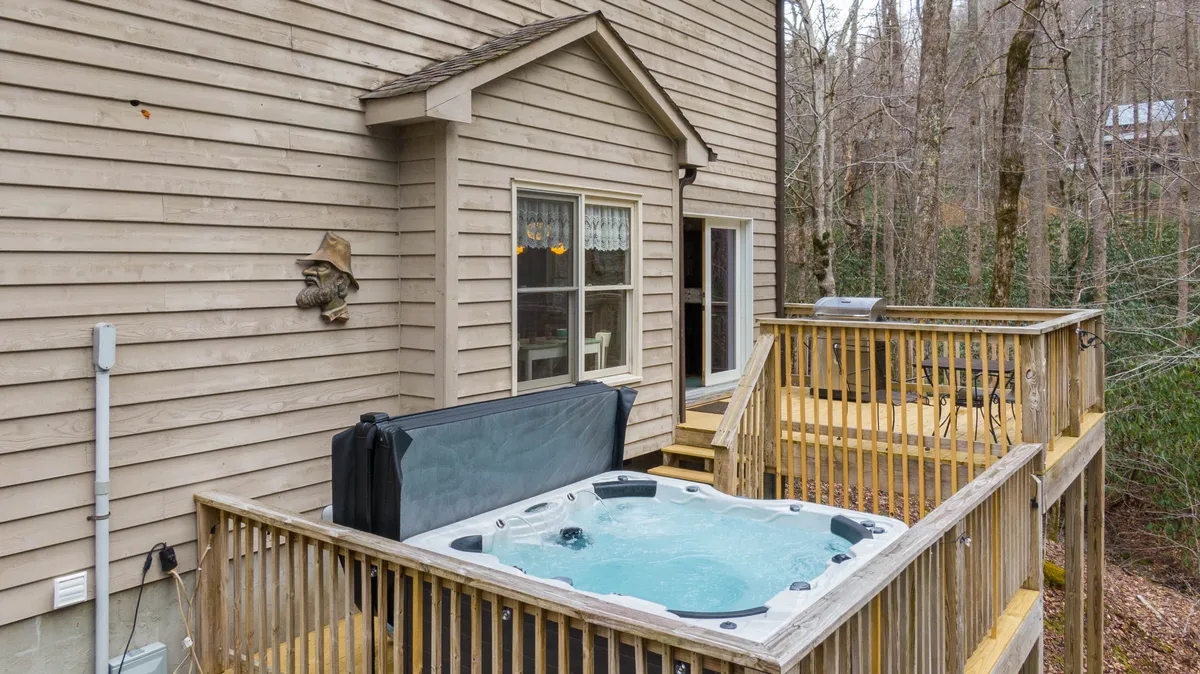 A view of the wooden deck featuring a hot tub, with the house’s exterior wall and towering trees in the background. The deck area is inviting for morning coffee or relaxing after a day of wine tasting, seamlessly blending indoor comforts with the outdoors.