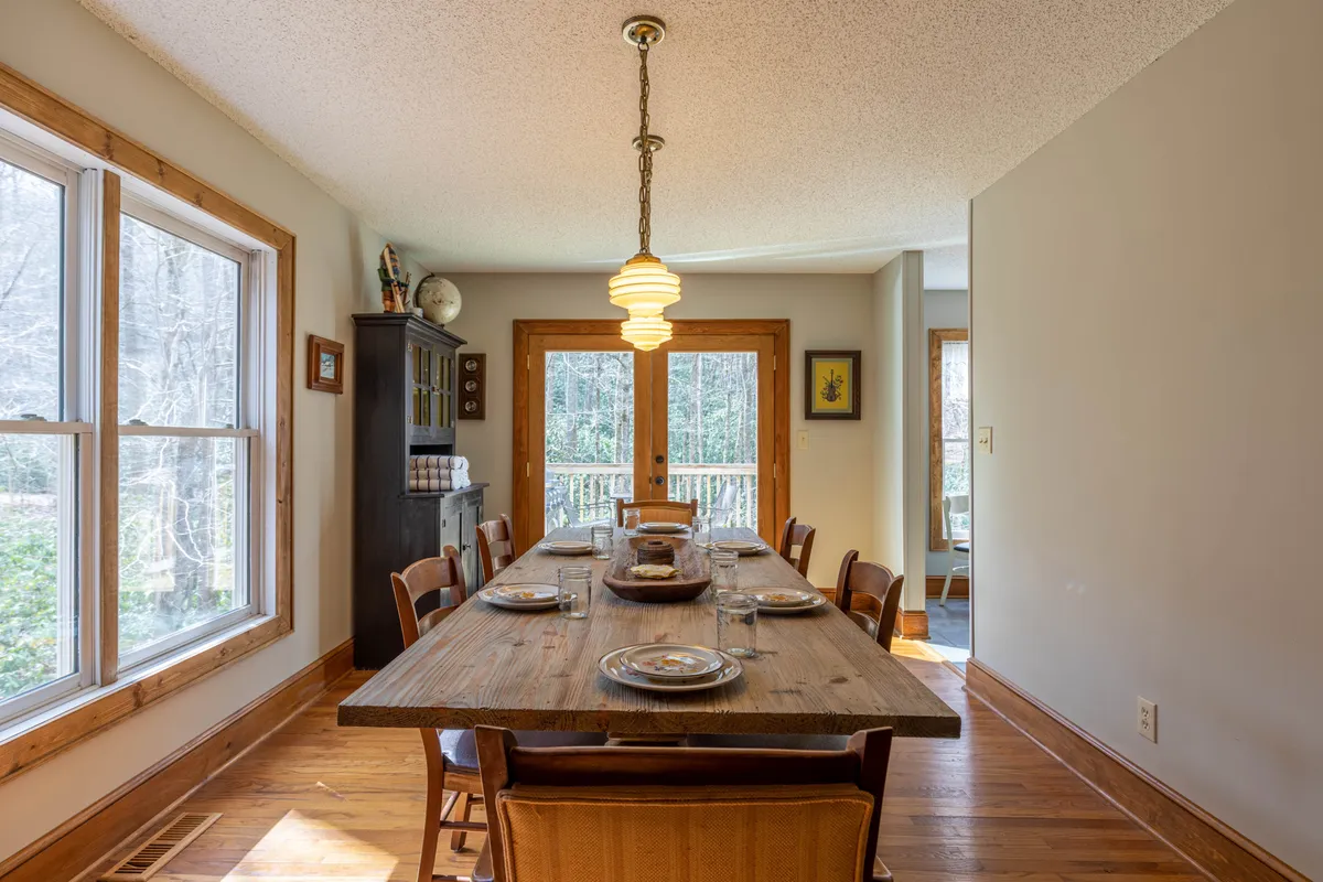 A dedicated dining space featuring a large wooden dining table surrounded by chairs, with double doors opening to the outdoors and a decorative cabinet in the background. The area is bathed in soft light and exudes a sense of warmth and welcome, inviting guests to linger over meals and conversation.