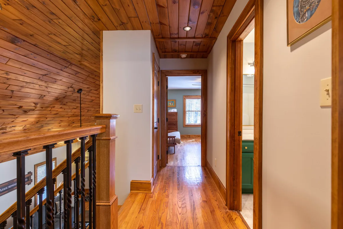 A wood-accented hallway with a natural wood ceiling, wooden railing, and doorways leading to other rooms. The inviting space feels both cozy and open, hinting at the warmth and togetherness found inside after braving the snowy conditions outside.