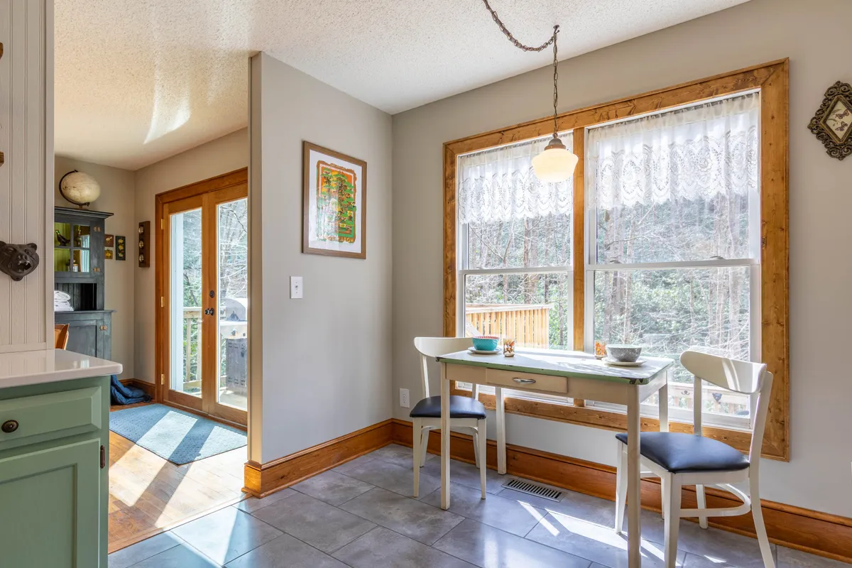 A bright and welcoming dining area featuring a spacious table set near large windows that fill the room with natural light. Decorative wall art adds character, while the view outside hints at the tranquil, scenic surroundings beyond. The ambiance is relaxed and perfect for gatherings after winter adventures.