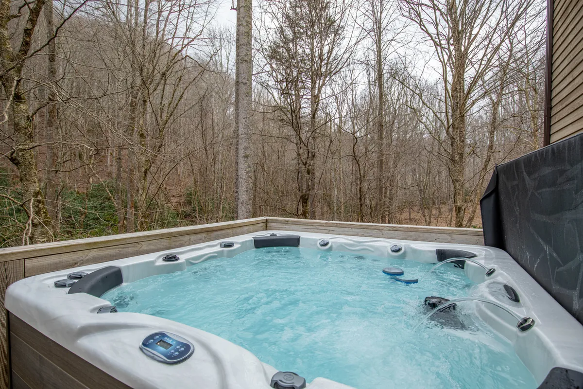 This image shows a private hot tub set on a deck surrounded by lush trees, creating a secluded and tranquil atmosphere. The hot tub invites guests to unwind and soak in the natural environment, with the deck providing ample space for relaxation or socializing outdoors.